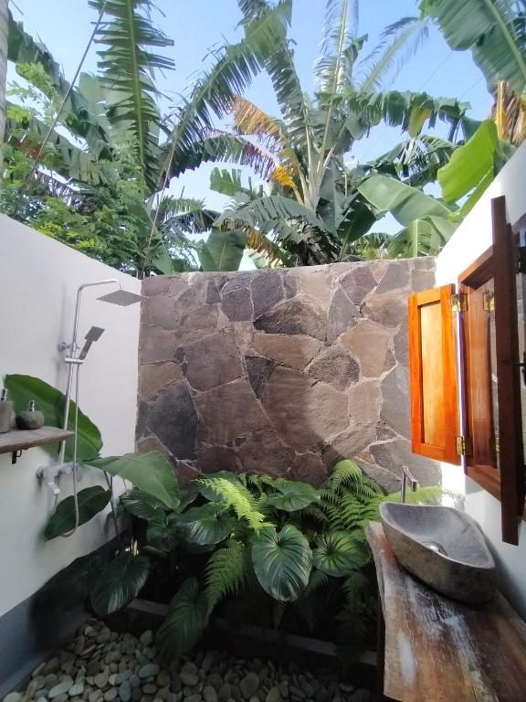 Outdoor stone shower surrounded by ferns and banana plants at The Geckos Homestay